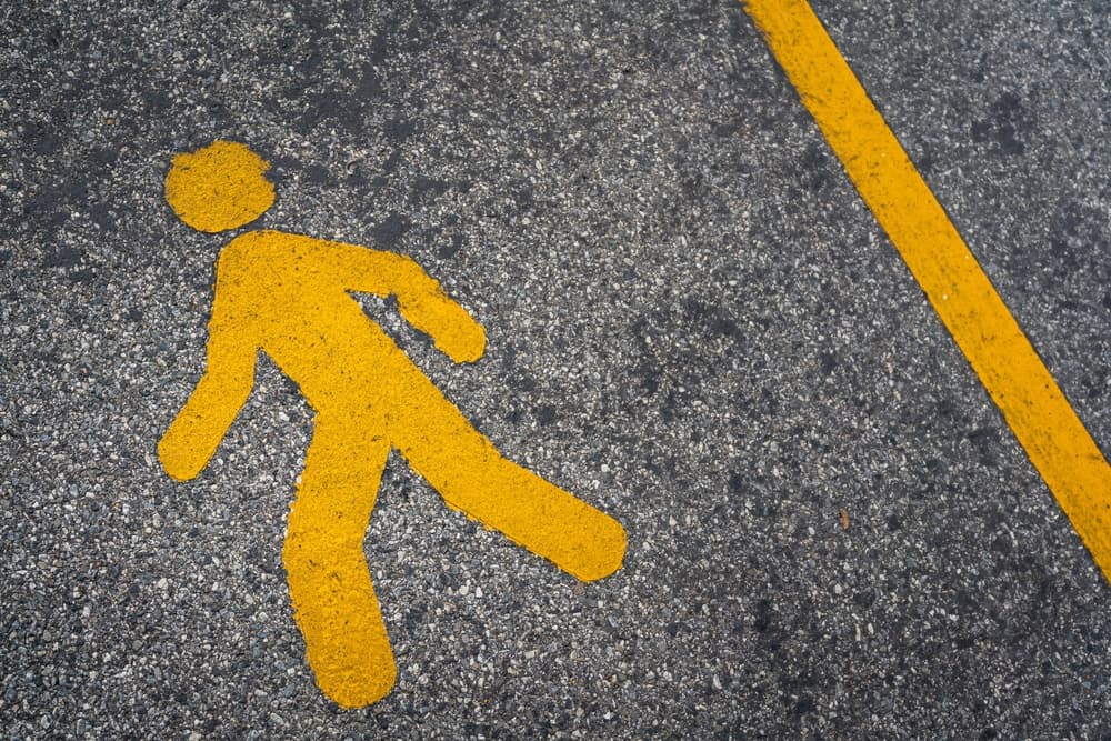 A pedestrian walking lane marked with a human icon on an asphalt road surface, representing a transportation symbol for safety background concept.