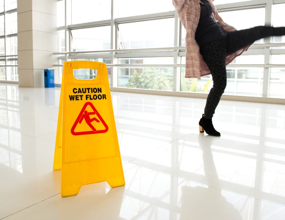 Woman slips beside wet floor sign.