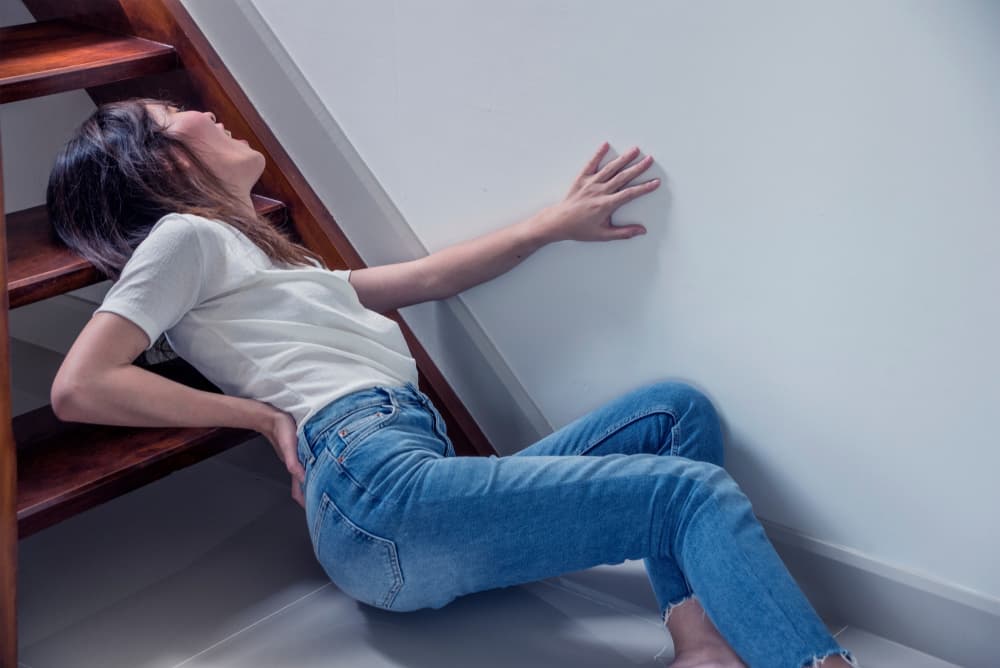 A woman experiences an accident by falling off the stairs, resulting in back pain or a potential back injury. This highlights the importance of home health insurance.