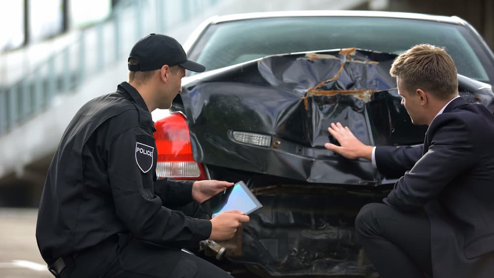 Insurance agent and police officer inspecting car damage at an accident scene, ensuring safety.






