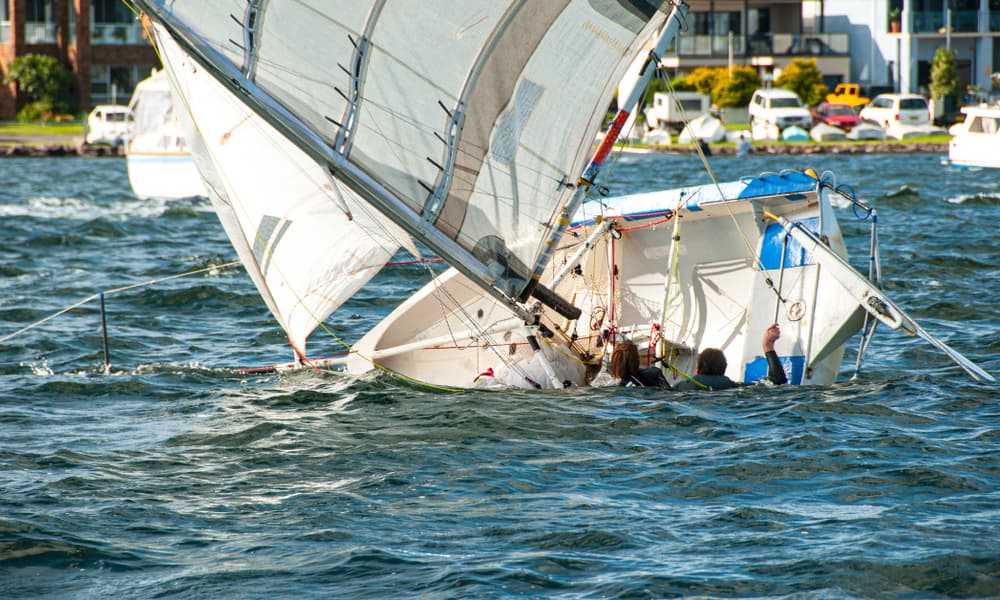 A girl and boy in the water climb back into a capsized racing sailboat. Teamwork by junior sailors on saltwater Lake Macquarie.