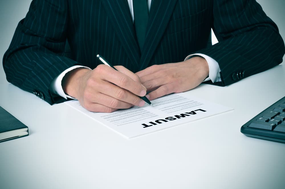 A lawyer in his office holds a document with the word "lawsuit" written on it.