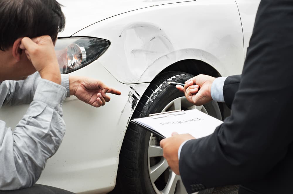 A senior man discusses the claim process with an insurance agent following a car crash, reviewing damage reports and policy coverage for compensation.