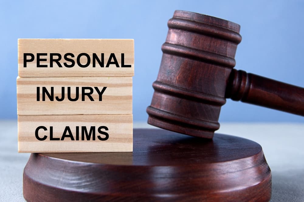 Wooden blocks spelling out "PERSONAL INJURY CLAIMS" are placed in front of a judge's gavel and stand, symbolizing legal proceedings. 