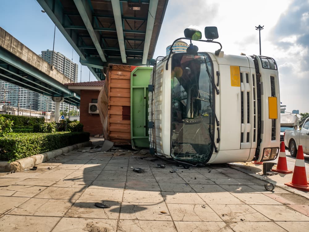 A truck transporting a container overturned on a road beneath a bridge at an intersection.






