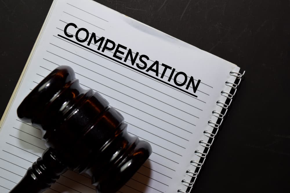 The word "Compensation" on a legal document next to a gavel, symbolizing law and justice, isolated on an office desk. Legal and compensation concept.