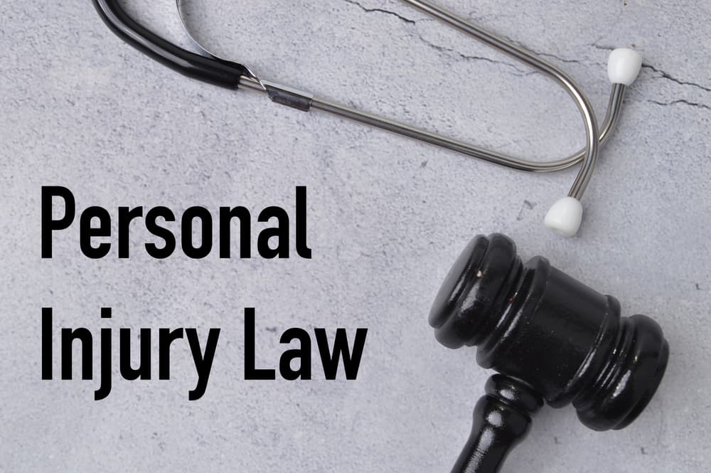 A top view of a stethoscope and judge's gavel placed on a grey background, with the text "PERSONAL INJURY LAW" written, symbolizing the intersection of healthcare and legal justice.