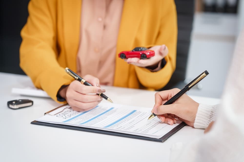 A businesswoman and a salesman are engaged in a discussion with a customer at a desk, focusing on car sales, insurance, and financing options.