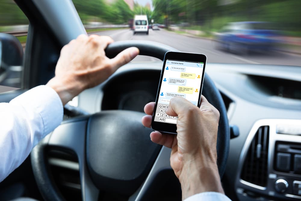 A Man's Hand Typing Text Message On Mobile Phone While Driving Car