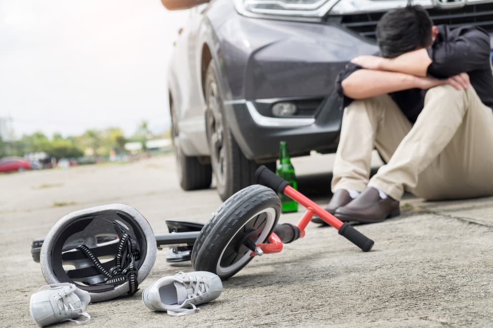 Scared and stressed desperate drunken driver and bottle of beer in front of automobile crash car with child bike after traffic accident in city road