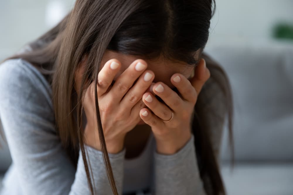 Unhappy young woman hiding face in hands, feeling upset after lost of loved one